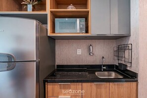 A compact kitchen with a refrigerator, microwave, sink, and wooden cabinets. - Studio in a Cond. With a Pool Near the sea Aru0123 (Salvador)