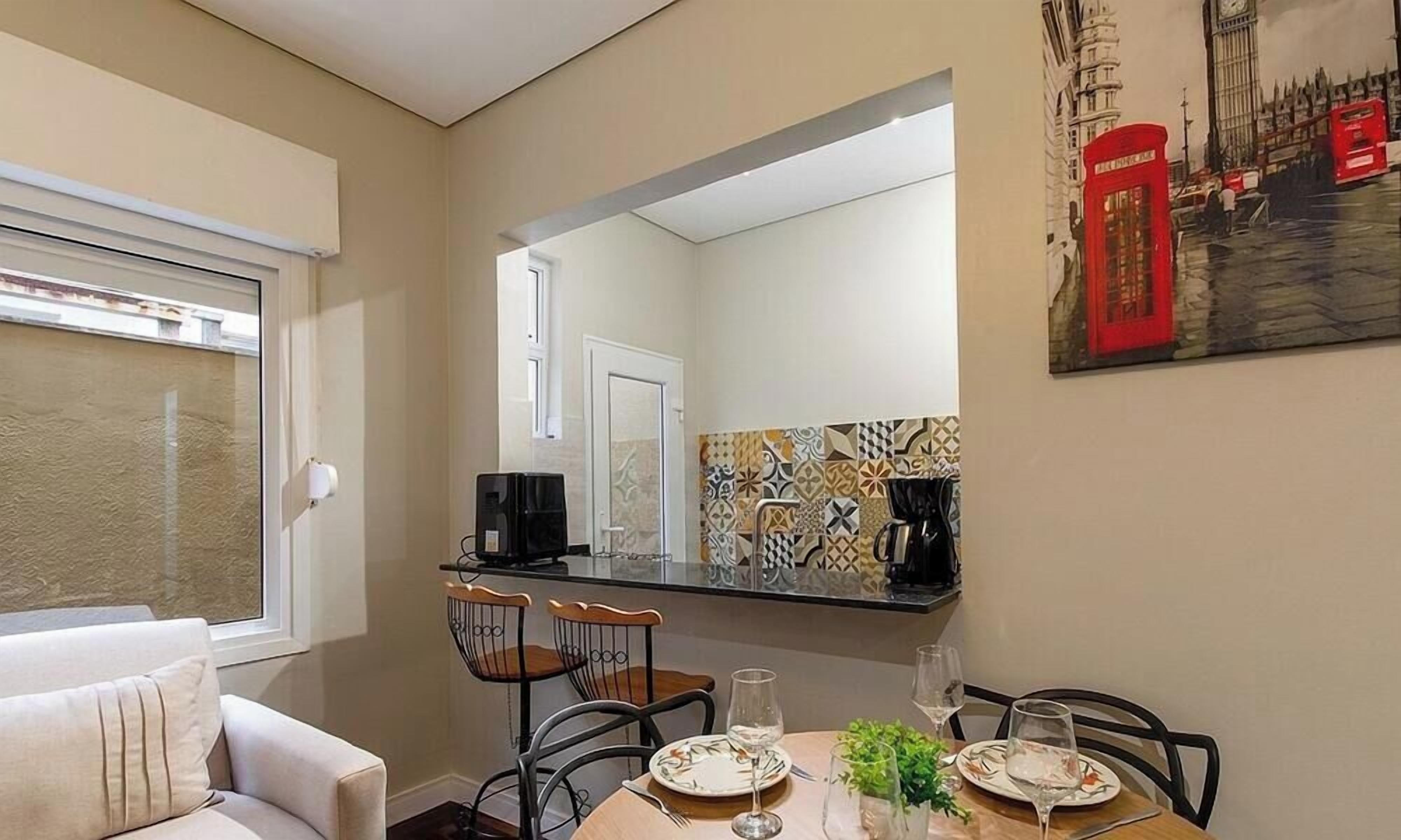 Uma área de refeições com uma mesa posta para dois, cadeiras, uma cafeteira e um quadro de uma cabine telefônica vermelha.
