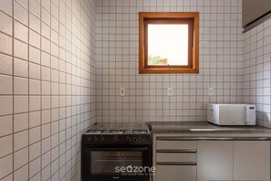 Eine Küche mit weiß gefliesten Wänden, einem Herd, einer Mikrowelle und einem Fenster mit Holzrahmen.