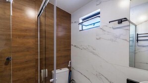 Un baño moderno con cabina de ducha de vidrio, pared de mármol y una pequeña ventana.