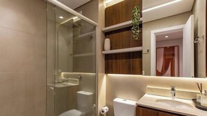 A modern bathroom with a glass shower enclosure, a toilet, a sink with a mirror above it, and wooden shelves with a plant. - Apt. w/ Fireplace & Balcony in Gramado Ohs0501 (Gramado)