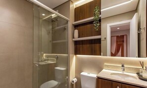 A modern bathroom with a glass shower enclosure, a toilet, a sink with a mirror above it, and wooden shelves with a plant. - Apt. w/ Fireplace & Balcony in Gramado Ohs0501 (Gramado)