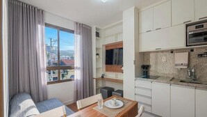 Ein kleines Hotelzimmer mit Essbereich, Küchenzeile und großem Fenster mit Vorhängen.