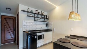 A modern kitchen with white subway tiles, black countertops, and a built-in oven. There is a black dishwasher and a hanging pendant light. - Apt. w/ City View in Downtown Piu0104 (Cabo Frio)