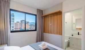 Ein Hotelzimmer mit großem Fenster, einem Bett, einem Holzschrank und einem Badezimmer mit Spiegel und Waschbecken.
