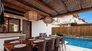 An outdoor dining area with wicker furniture and hanging lights, a pool, and a wooden fence. - House w/ Private Pool in Alto da Pitinga Ptg0003 (Porto Seguro)