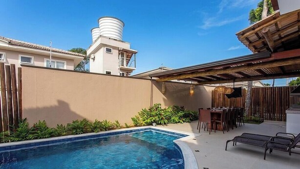 A swimming pool with a covered patio area, a dining setup, and a water tank on a building. - House w/ Private Pool in Alto da Pitinga Ptg0003 (Porto Seguro)