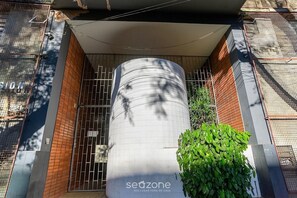 A cylindrical structure with the text 'sedzone' and 'SEU LUGAR FORA DE CASA' on it, surrounded by a brick wall and metal gates. - Studio in Front of Befly Hall Sio0302 (Belo Horizonte)