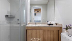 Een moderne badkamer met een glazen douchecabine, een houten wastafelmeubel met een wastafel en een spiegel die uitkijkt op een keuken.