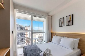 A hotel room with a large bed, a balcony with a view of the city, and two framed artworks on the wall. - Sophisticated Studio in a Cond. With a gym Man1707 (Curitiba)