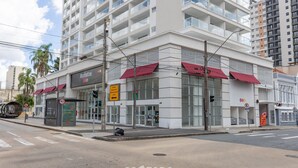 Een modern gebouw met een commerciële begane grond, met daarin een restaurant genaamd "Manhattan Love" met rode luifels, en een zichtbaar bord met een snelheidslimiet van 40 km/u.