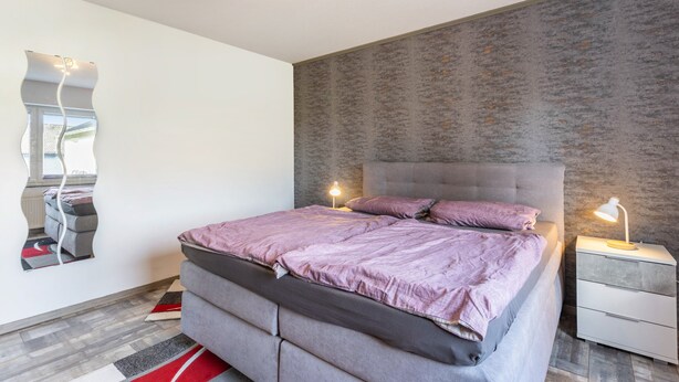 Een moderne slaapkamer met een groot bed, een nachtkastje, een spiegel en een gestructureerde wand.