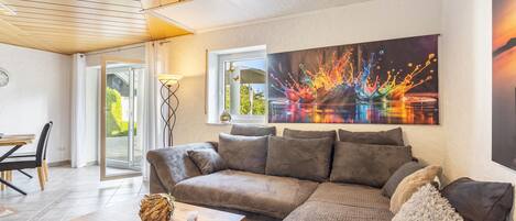 A modern living room with a wooden ceiling, a large painting, a sofa, a coffee table, and a dining area with chairs.