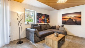 Een gezellige woonkamer met een hoekbank, een salontafel, een vloerlamp en twee schilderijen aan de muur.