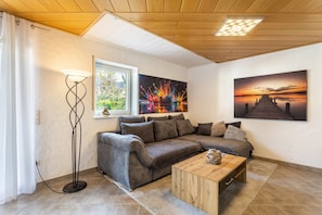 Ein gemütliches Wohnzimmer mit einem Ecksofa, einem Couchtisch, einer Stehlampe und zwei Bildern an der Wand.