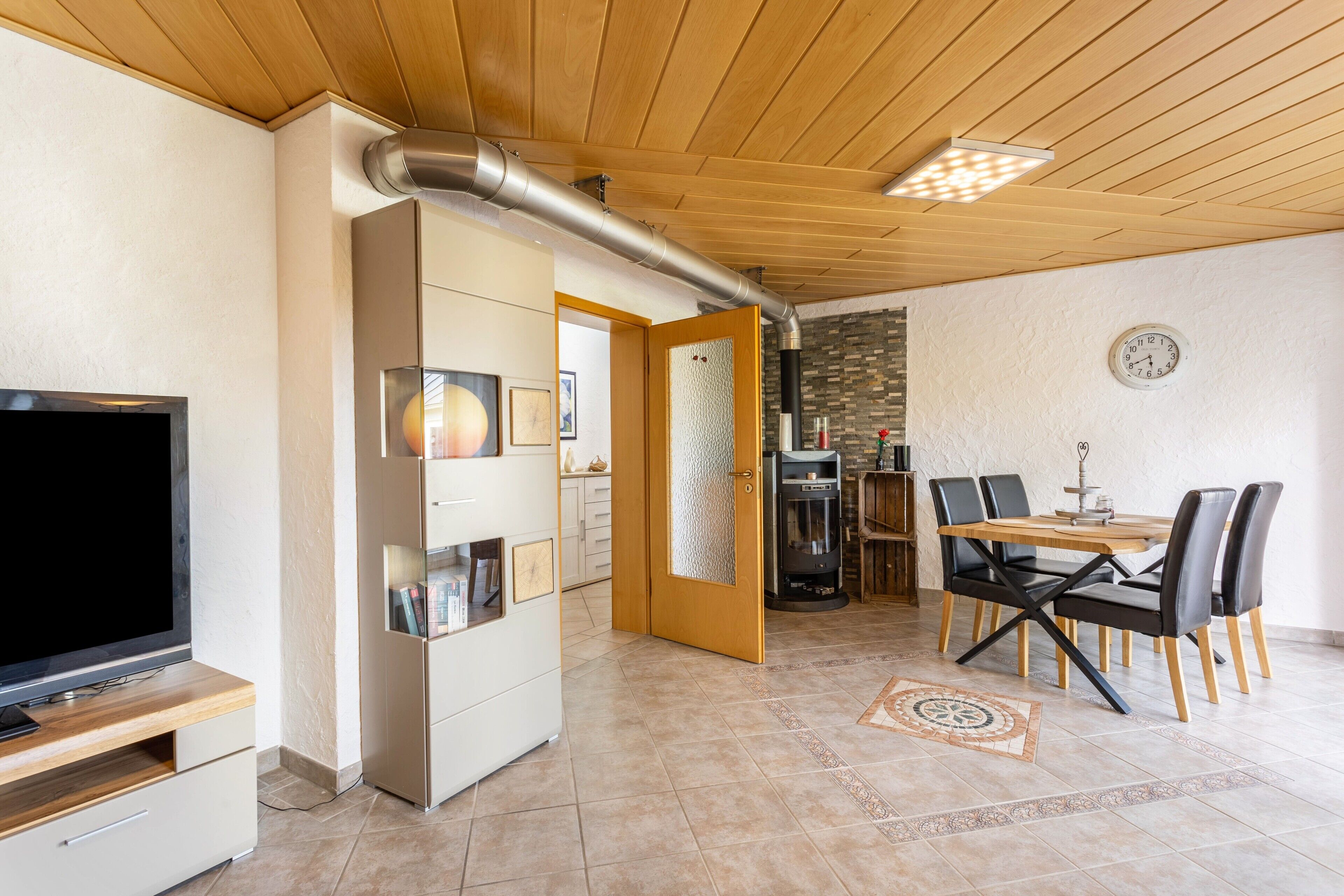 Ein modernes Wohnzimmer mit Fernseher, einer Essecke mit Tisch und Stühlen sowie einem Kamin.