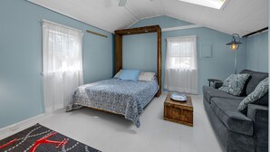 A bedroom with a four-poster bed, a grey sofa, a wooden chest of drawers, and a skylight. - Cozy pet-friendly 1-bedroom cottage near the beach in beautiful Truro with AC (Truro)