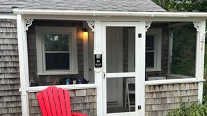 A house with a porch, a red chair, and a doormat with 'hello sunshine' written on it. - Cozy pet-friendly 1-bedroom cottage near the beach in beautiful Truro with AC (Truro)