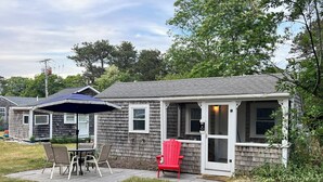 A single-story house with a covered patio area, a dining table, and outdoor seating. - Cozy pet-friendly 1-bedroom cottage near the beach in beautiful Truro with AC (Truro)