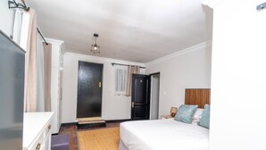 A bedroom with a bed, a nightstand, a door, and a hanging light fixture. - Room-single Rooms With Shared Bathroom 2 (Johannesburg)