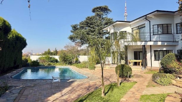 A modern two-story house with a swimming pool, a balcony, and a view of a tall tower. - Room-single Rooms With Shared Bathroom 2 (Johannesburg)