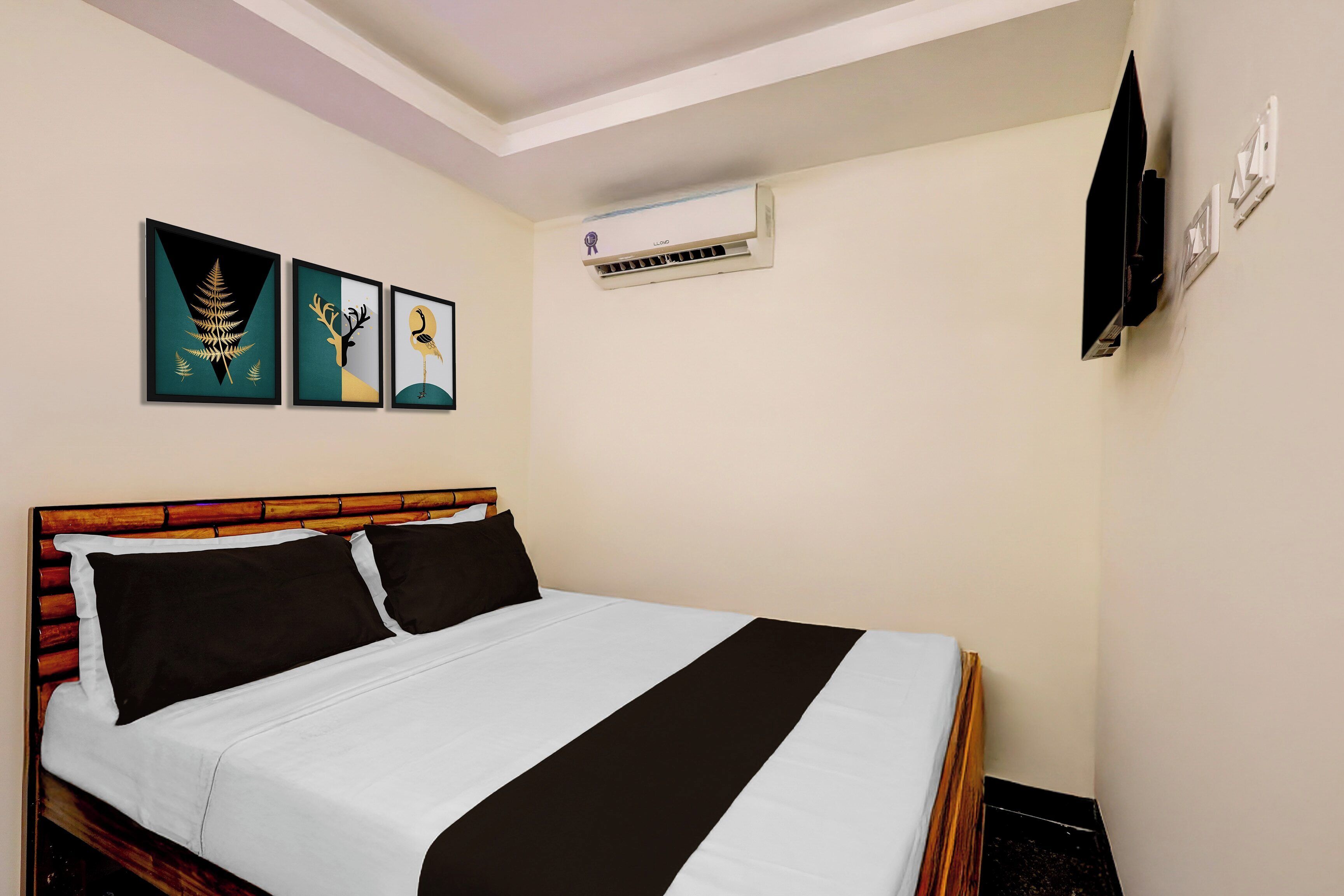 A hotel room with a bed, a wall-mounted air conditioner, and three framed artworks.