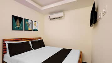 A hotel room with a bed, a wall-mounted air conditioner, and three framed artworks.