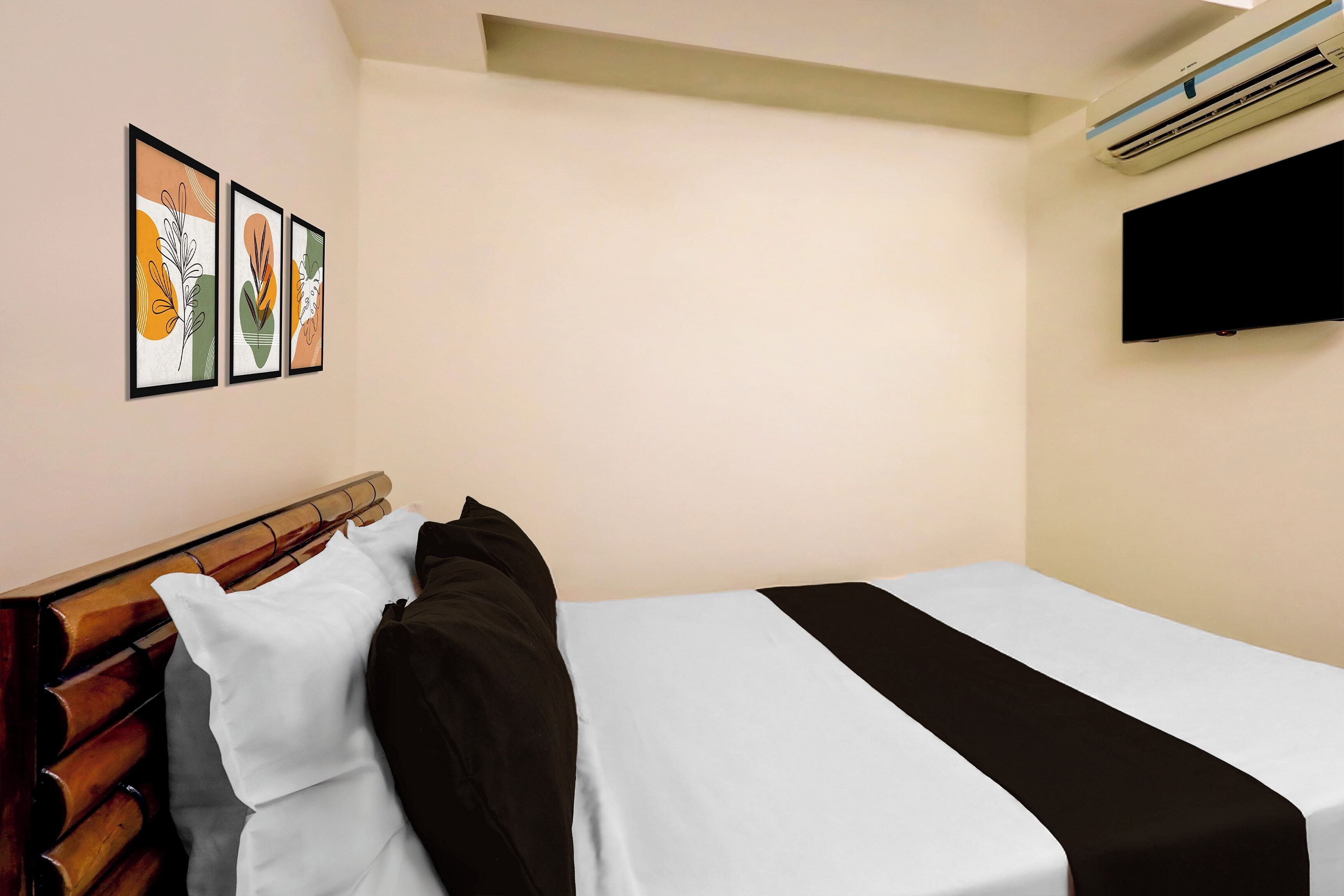 Una camera d'albergo con un letto, una TV a schermo piatto montata a parete e due opere d'arte incorniciate.