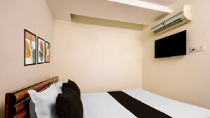 Een eenpersoonsbed met houten hoofdbord, een flatscreen televisie aan de muur bevestigd en een airconditioner in het plafond.