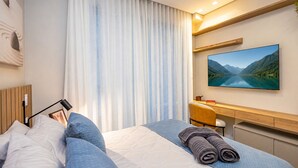 Ein Hotelzimmer mit einem Bett, einem Schreibtisch, einem Stuhl, einem Gemälde und einem Fenster mit Vorhängen.