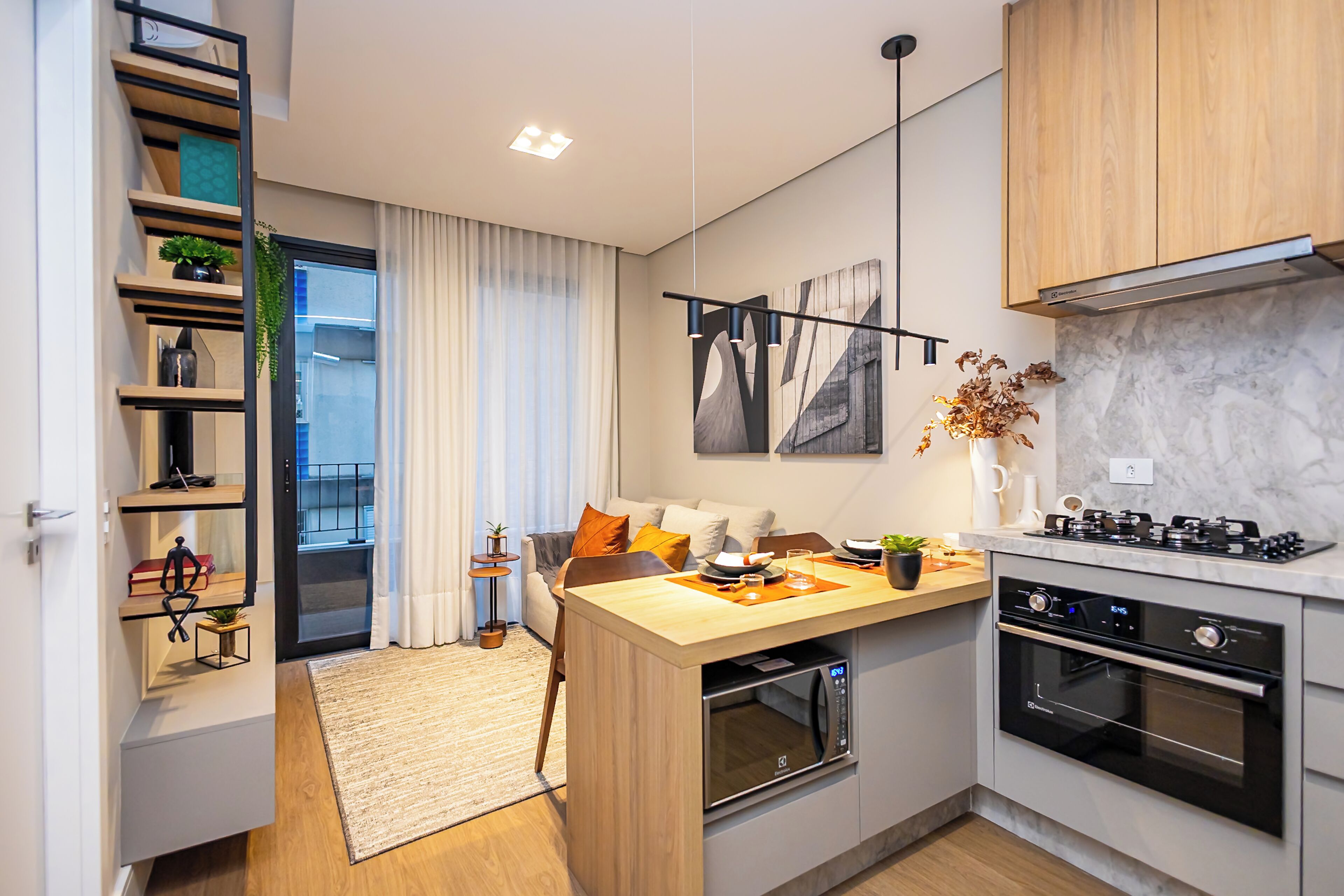 A modern kitchen with a built-in oven, a stove, and a microwave. There is a dining area with a table and chairs, and a small side table with a plant.