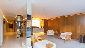 Eine moderne Hotelhalle mit Empfangstresen, Sitzgelegenheiten und einer Glastrennwand.