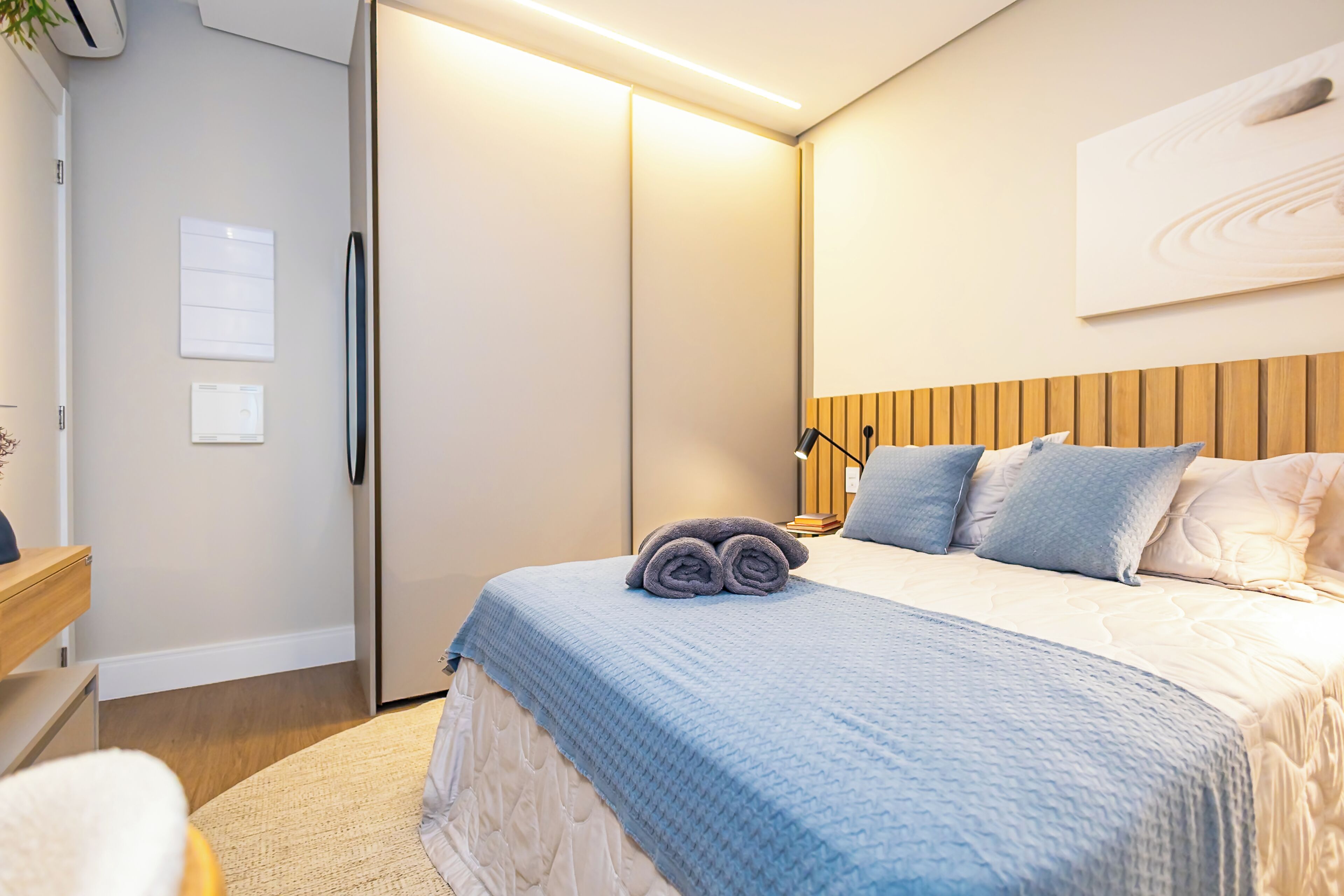 A hotel room with a bed, a bedside table, a wardrobe, and a wall-mounted artwork.