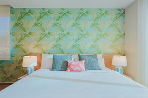 Ein Hotelzimmer mit einem Bett, zwei Nachttischlampen und Tapete mit tropischem Blattmuster.
