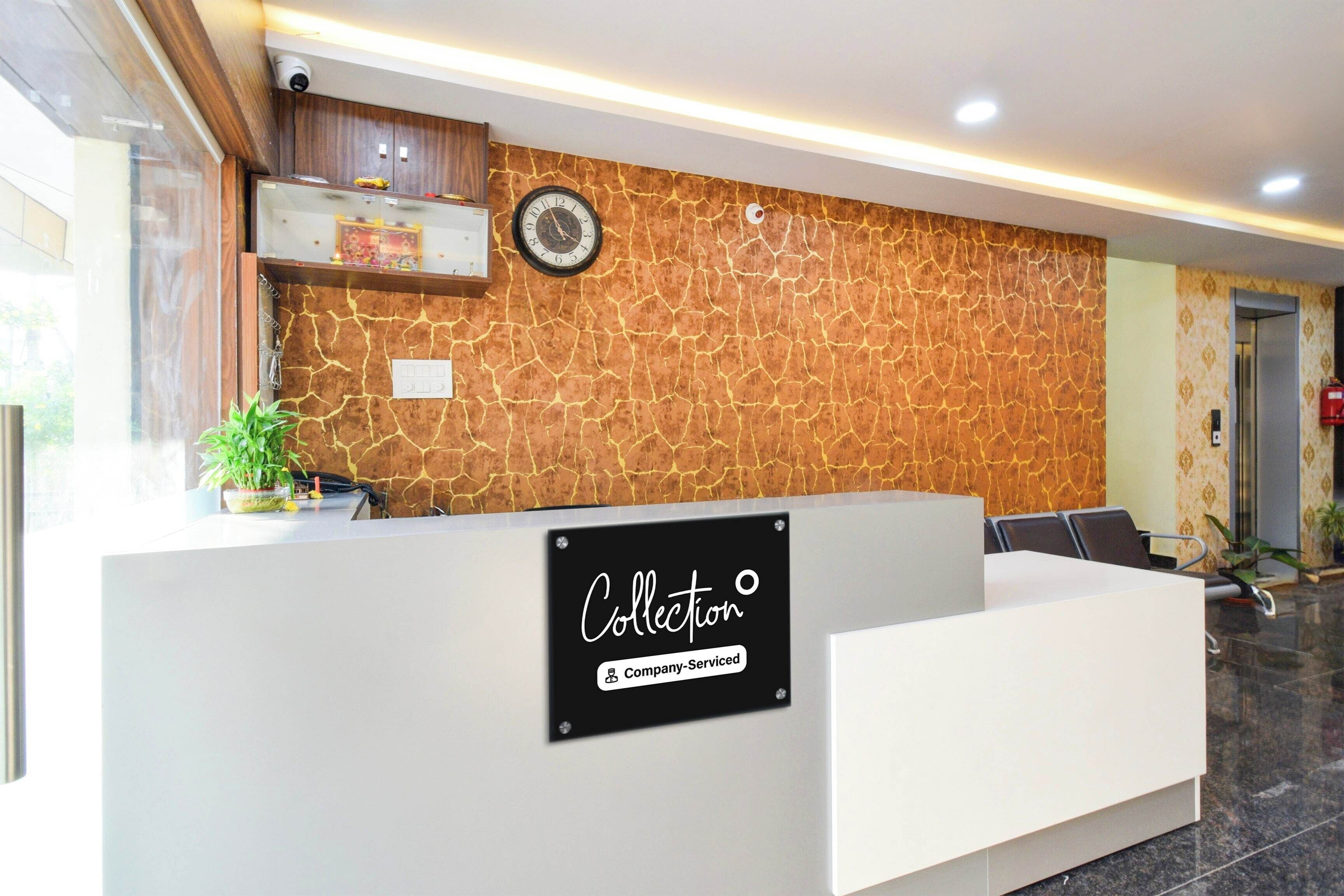 Taulell de recepció amb un cartell que indica que ofereix servei de l'empresa. Hi ha un rellotge a la paret i una planta sobre la taula.