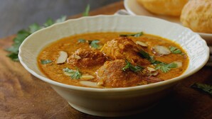 Un tazón de curry con albóndigas, adornado con hierbas, acompañado de panecillos.