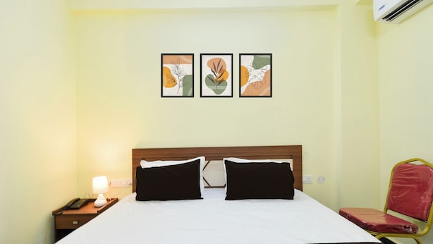 Habitación de hotel con cama, dos almohadas negras, mesita de noche con lámpara, teléfono y aire acondicionado de pared.
