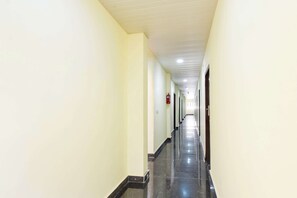 Un pasillo largo y estrecho con paredes de tonos claros y piso oscuro, que lleva a una puerta al final.
