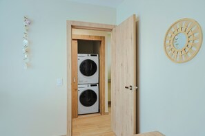 Un lavadero con dos lavadoras y secadoras apiladas, una puerta de madera y un espejo instalado en la pared.