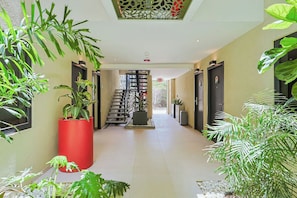 A hotel corridor with a staircase, potted plants, and a modern ceiling design. - Bonsai Studio-Tranquil 103 (Noord)
