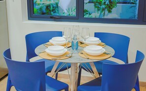 A dining table set with white plates, clear glasses, and a blue vase, surrounded by blue chairs. - Bonsai Studio-Tranquil 103 (Noord)