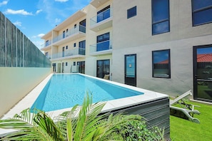 A modern building with a swimming pool, balconies, and a well-maintained lawn. - Bonsai Studio-Tranquil 103 (Noord)