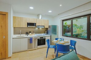 A modern kitchen with stainless steel appliances, a dining area with blue chairs, and a window with a view of greenery. - Bonsai Studio-Tranquil 103 (Noord)