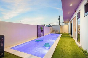 A modern outdoor pool area with a clear sky, a green lawn, and a purple wall. - Bonsai Studio-Serenity 108 (Noord)
