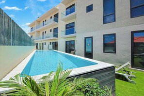 Un edificio moderno con piscina, balcones y un césped bien cuidado.