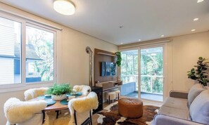 A modern living room with a flat-screen TV, a dining table with chairs, a sofa, and a large window with a view of trees. - Ap Cathedral of Stone Street w/ Fireplace Mde0407 (Canela)