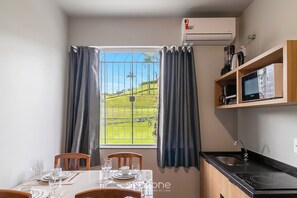 A kitchen with a dining area, a window with curtains, and an air conditioning unit. - Apt. w/ Parking & City View Ola0003 (Blumenau)