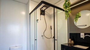 A modern bathroom with a glass-enclosed shower, a toilet, and a black countertop with a sink and mirror. - Studio in Condo. w/ Pool and Balcony Rso0040 (Imbituba)