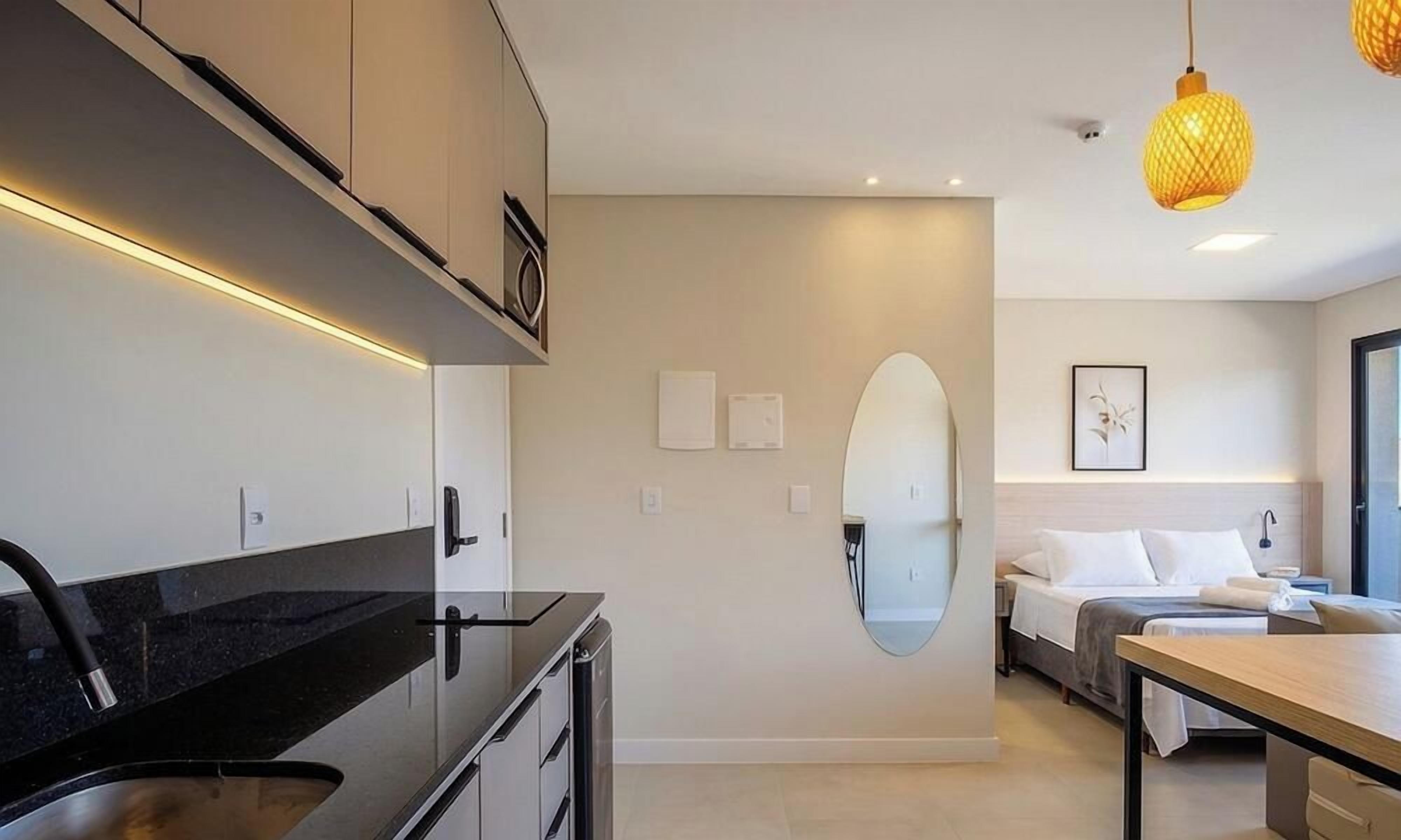 Une cuisine moderne avec un plan de travail et des placards noirs, un coin repas avec une table en bois, et une chambre avec un lit et une table de chevet.
