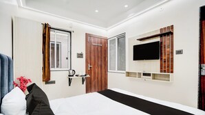 Een moderne hotelkamer met een bed, een aan de muur bevestigde televisie, een houten deur en een raam met gordijnen.